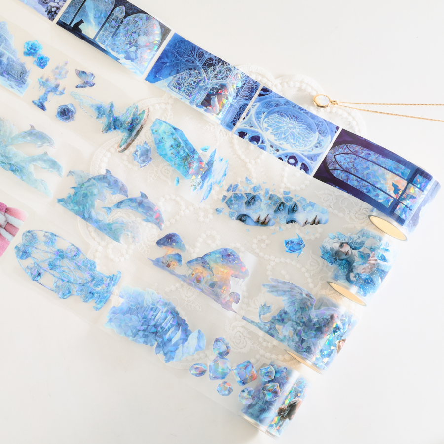 A quiet studio is bathed in the soft amber glow of a desk lamp, where a creator carefully peels a strip of translucent tape, its surface shimmering with delicate floral patterns and metallic accents