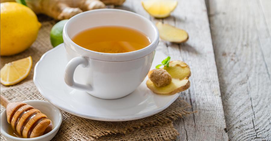 Photograph showing a cup of freshly brewed tea, with a small bowl of honey and slices of fresh ginger, lemon and lime.
