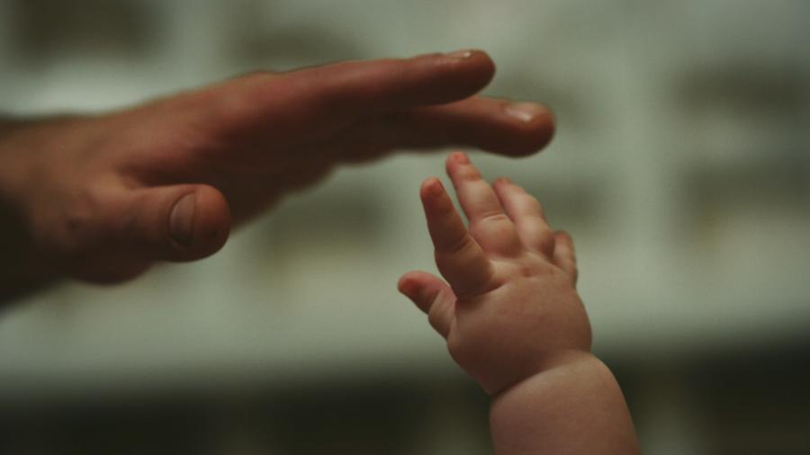 Photograph of an adult hand and an infant's hand touching.