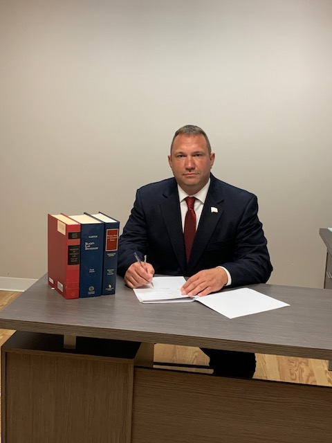 Eric Kaasa in Suit at Desk with Law Books and American Flag Pin