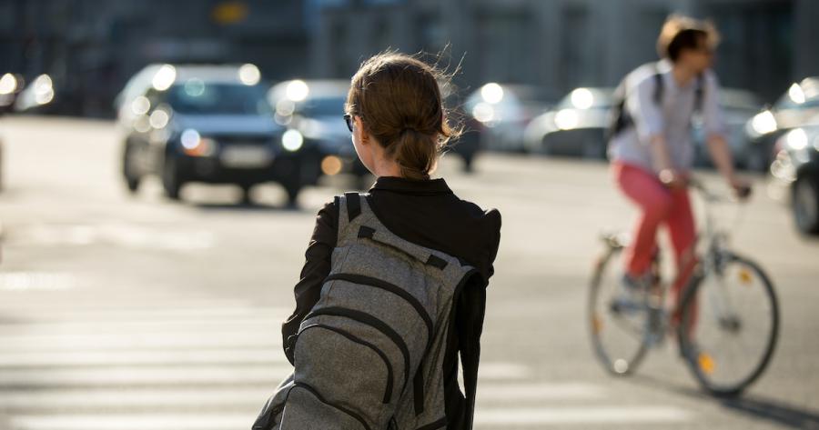 Young Woman with backpack crossing the street with traffic in the background