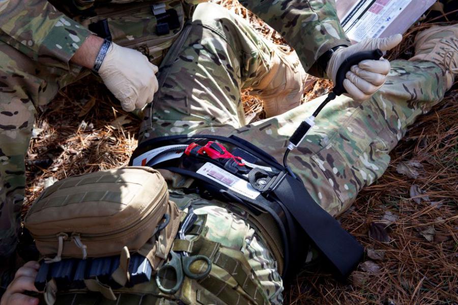 A combat medic applies the AAJT-S device to a patient's abdomen in a battlefield environment to control non-compressible torso hemorrhage and stop life-threatening bleeding.