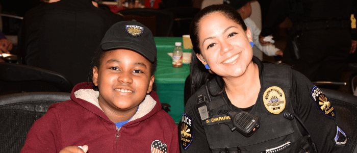 The International Board of Credentialing and Continuing Education Standards (IBCCES) recognizes the Goodyear Police Department as a Certified Autism Center™ (CAC) after completing an autism-specific training and certification process woman Goodyear police officer sitting with young black boy at an event