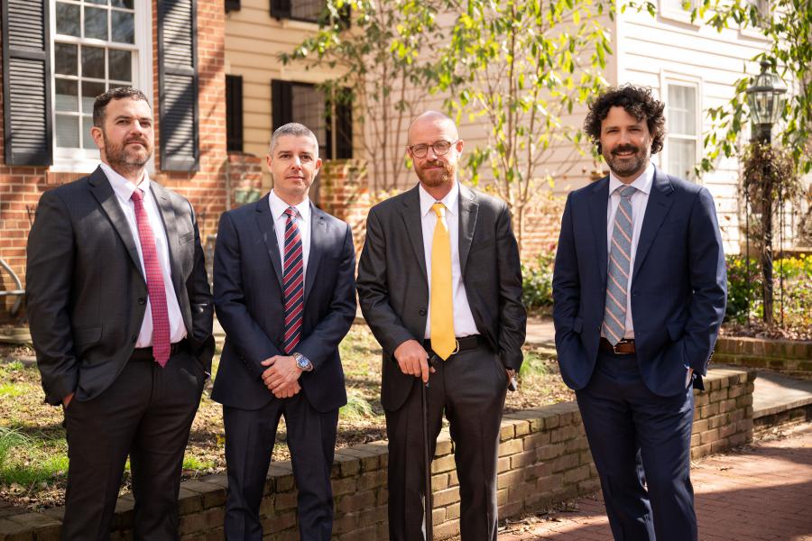 The four lead attorneys of Werner, Hoffman, Greig & Garcia stand on a street in Washington DC facing the camera