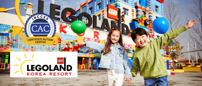 A young girl and boy smiling while holding hands in front of LEGOLAND Korea Resort entrance.