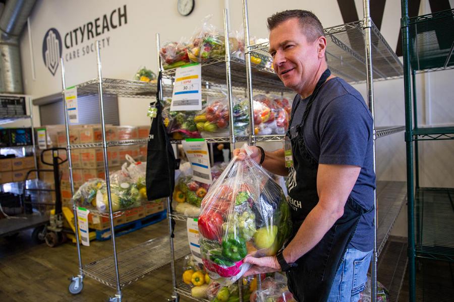 Tom Truchan is at CityReach standing in front of shelves with fresh produce holding bags of food.