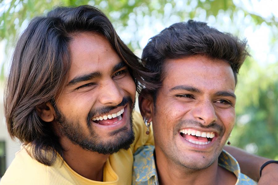 Two joyful LGBTQ men from India, smiling and embracing, celebrating their relationship in a setting that reflects their culture.