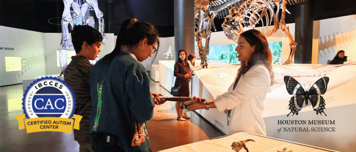 A museum educator engages with two visitors, showcasing a small exhibit at the Houston Museum of Natural Science, which is recognized as a Certified Autism Center™ by IBCCES.