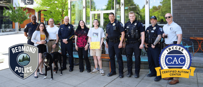 A group photo of Redmond Police Department officers and community members standing together, featuring the Redmond Police and IBCCES Certified Autism Center™ logos.