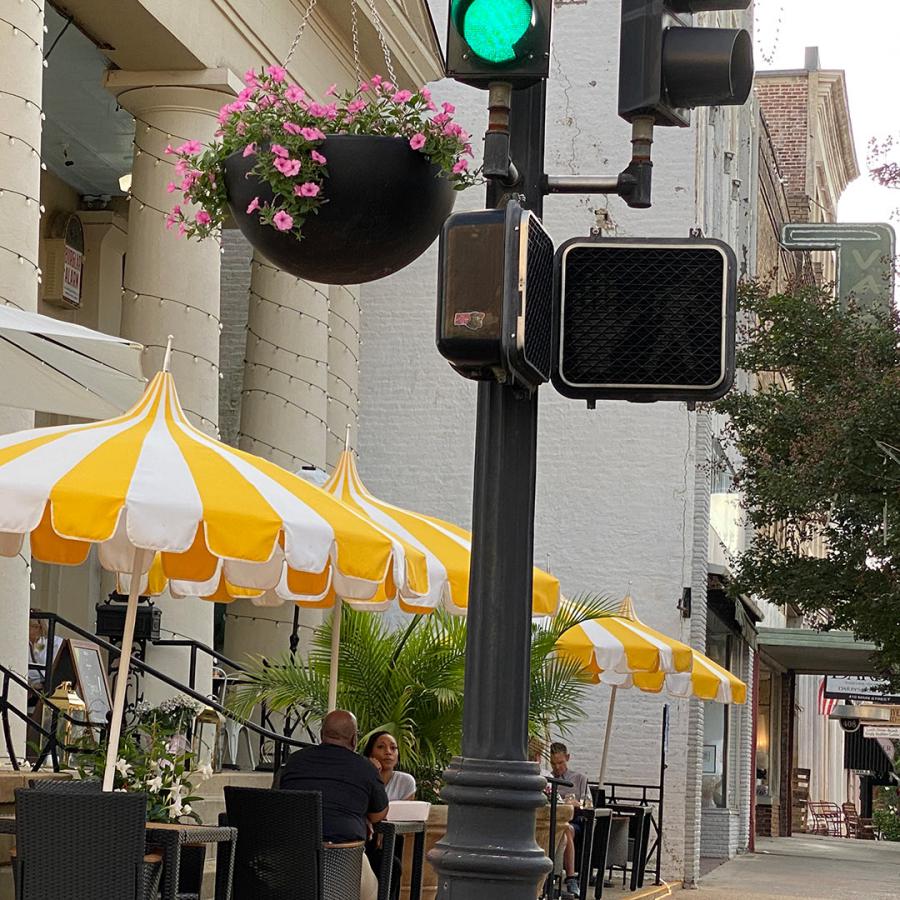 A stoplight at Main and Commerce Streets in Downtown Natchez. Patrons can be seen at the outside dining area with yellow & white umbrellas at the restaurant, Frankie's On Main.