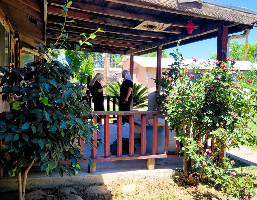 two sisters standing talking on a wooden porch with rose bushes in the foreground