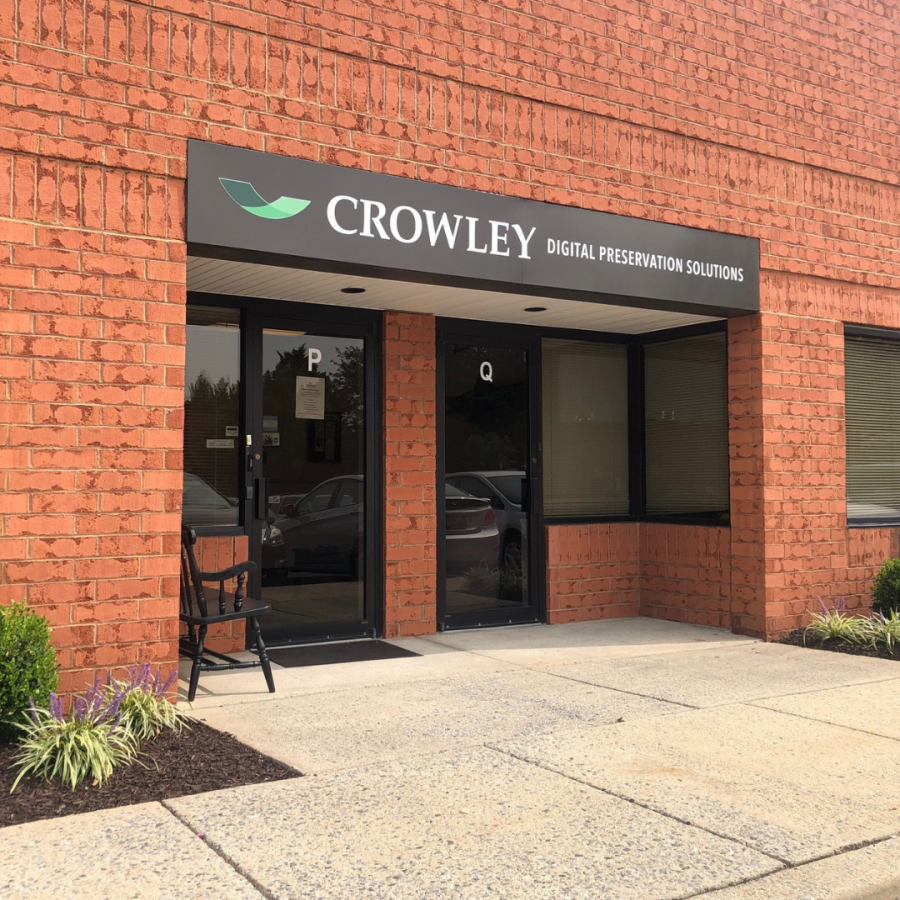 Photograph of a brick building with black doors and a black sign depicting The Crowley Company's logo