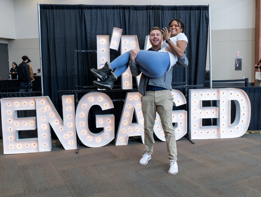 A recently engaged couple celebrates with a playful photo in front of a lit “ENGAGED” sign, capturing the joy and excitement of the event.