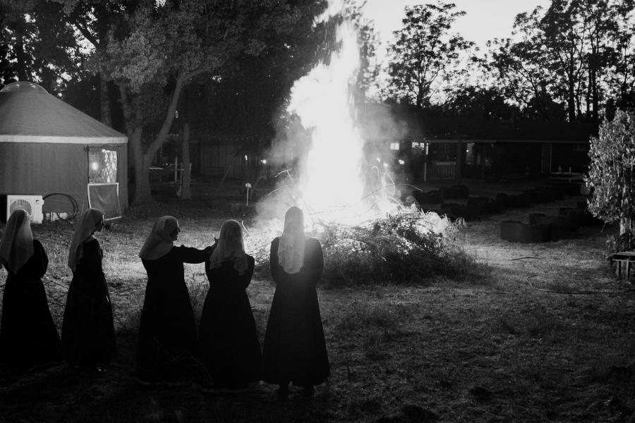 four nuns (from the back side) standing by a fire circle at night