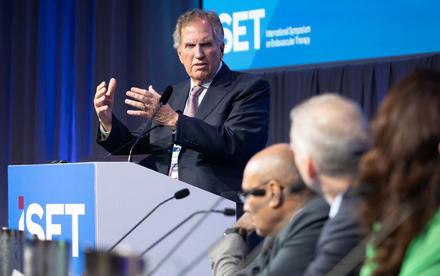 Barry Katzen speaks at a lectern with an august panel of experts in the foreground.