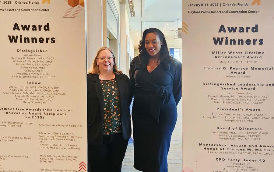 Two women stand between signs at a conference.