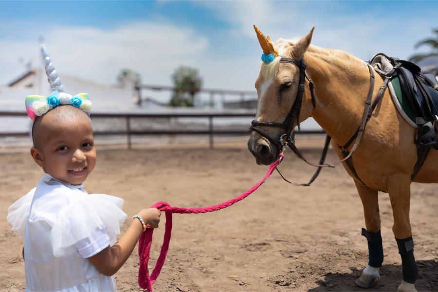 A young girl wearing a unicorn headband leads a horse with a unicorn horn