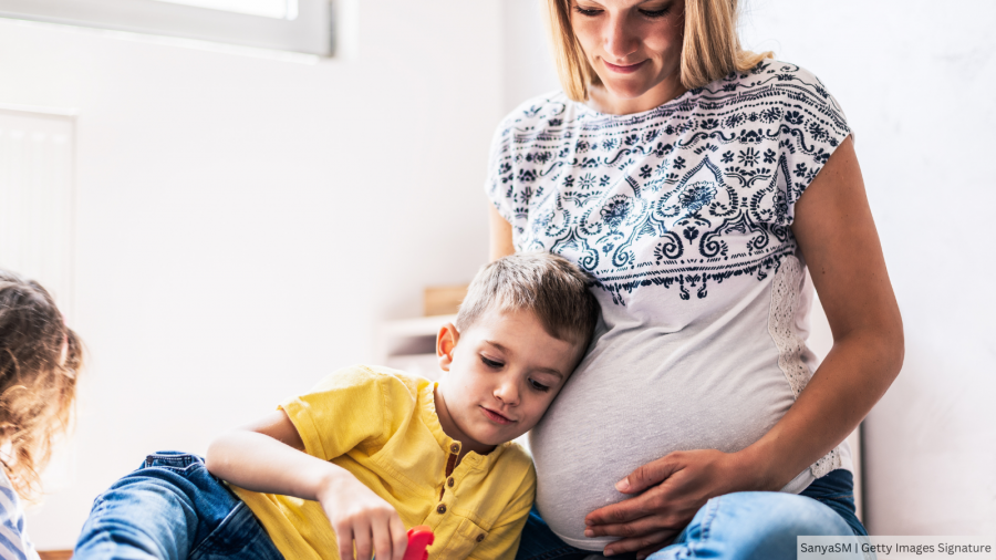 Pregnagnt person with hand on stomach while child rests and plays nearby