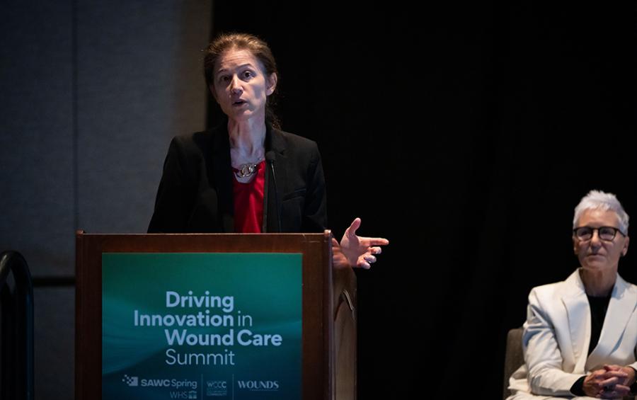 Woman speaking at a podium with another woman in the background