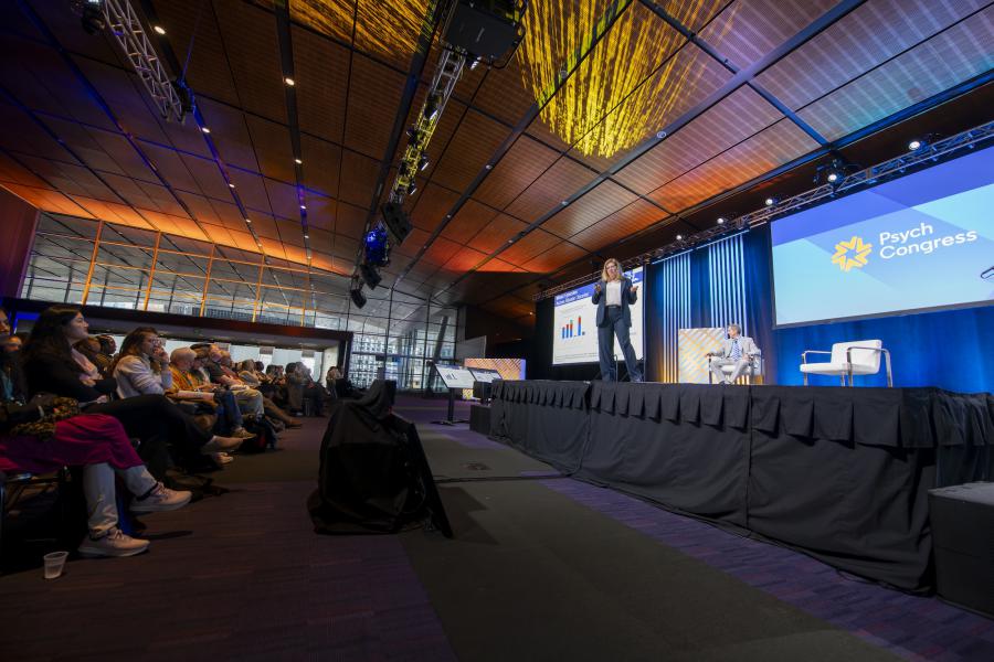 Woman speaking on a stage in front of a full room of conference attendees