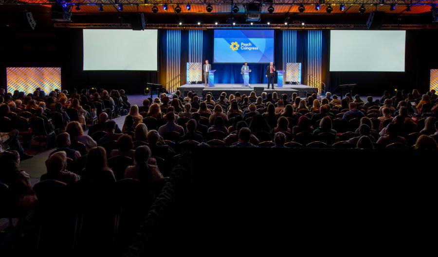 Full room of conference attendees watching a presentation on the main stage