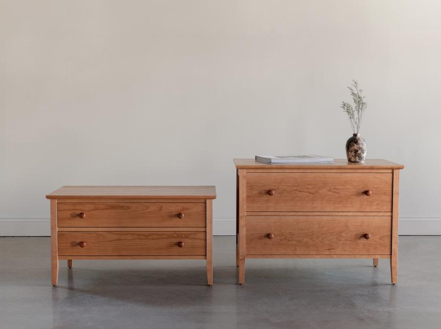 Two Shaker inspired, cherry wood, bedroom storage chests sitting side by side in an empty room, with two drawers each, one styled with a book and vase