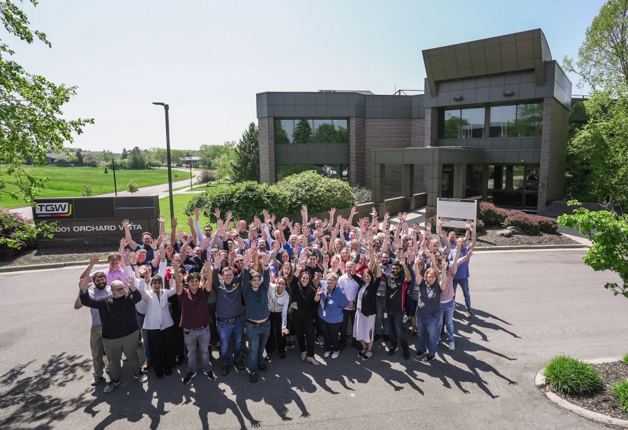 Some of the 300 employees of TGW North America, a strong warehouse automation partner, outside their headquarters with arms raised