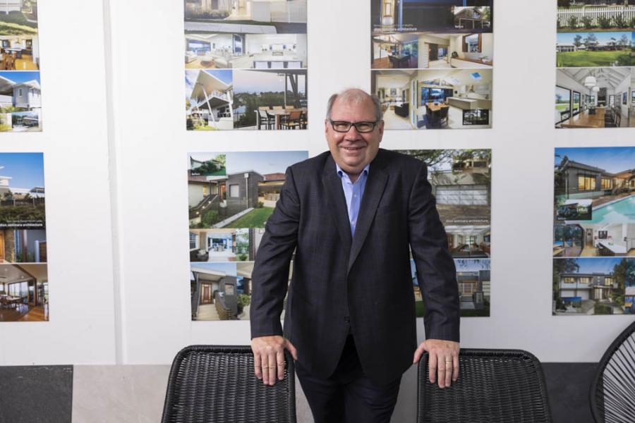 Dion Seminara standing in front of completed project images at the dion seminara architecture studio, representing flexible architectural service offerings.