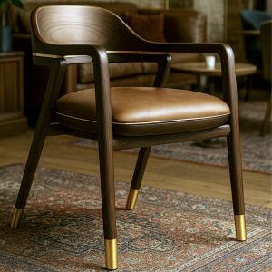 Angela Chair in dark walnut with leather seat and brass-capped legs, photographed in a warm, heritage-inspired lounge setting.