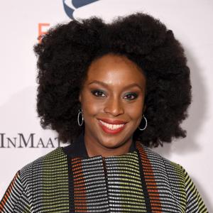 Chimamanda Ngozi Adichie smiling to camera against wall with Equality Now logos