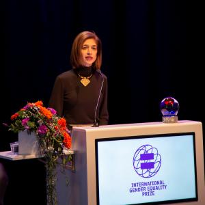 Equality Now's Yasmeen Hassan standing behind a podium on stage at Finnish Government's Gender Equality Prize  Ceremony 2019 speaking into a microphone to accept the