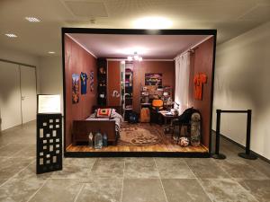 A life-sized recreation of a Ukrainian child's bedroom, displayed as an open room installation in a modern building. The room contains a bed, desk, wardrobe, sports memorabilia, and stockpiled water bottles — frozen at the moment of a child's abduction in