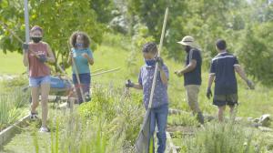 Several young adults and children holding rakes tend to ARECMA's garden.