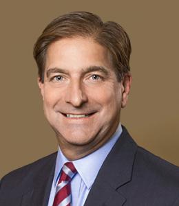 Headshot of a middle-aged white man wearing a suit and tie with brown hair and brown eyes.