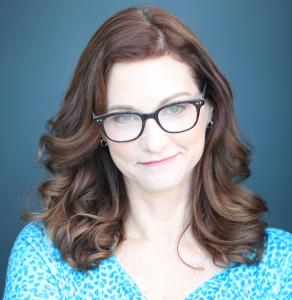 headshot of Lori Hamilton a woman with a blue and white dress and red hair who is wearing glasses