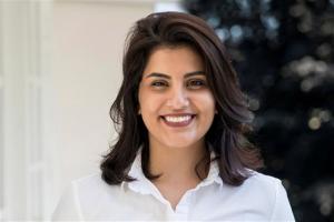 Photograph of Saudi women's rights defender Loujain Al-Hathloul, head shot, Loujain smiling and looking directly to the camera, dark shoulder length hair and white shirt
