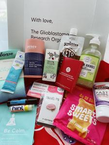 White box opened with several products inside such as hand sanitizer, peanut butter pouch, pins, stickers, socks, and beauty products.