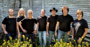 Members of The Outlaws stand against a wall, with all seven wearing black t-shirts.
