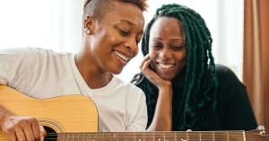 African-American woman playing guitar to her female lovers as they chilling at home.