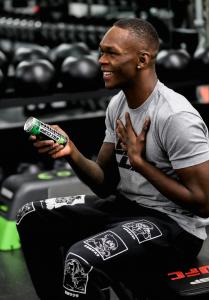 Israel Adesanya smiling in a Kill Cliff shirt with a Kill Cliff drink can