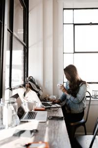 woman holding coffee, working on a laptop at desk in well lit room