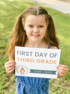 Young girl holding a 'first day of 3rd grade' sign with Ignite Learning Academy's logo.