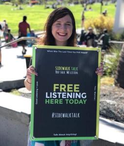 Young woman holding free listening sign for Sidewalk Talk Listening Project