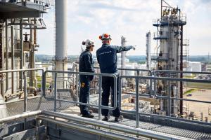 Haldor Topsoe technicians stand on top of a big chemical plant, one of them pointing at a silo installation