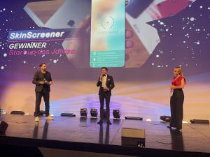 SkinScreener wins Start-up-of-the-Year by futurezone. The picture shows Phlipp Efferl, who represented SkinScreener, and two moderators on stage. In the background, the SkinScreener app is shown.