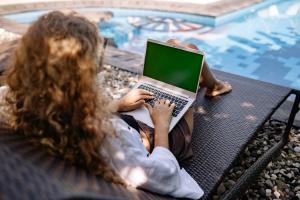 A woman with a laptop, on a sun lounger next to her villa's pool.