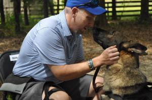 White male in a blue striped shirt gets a kiss from a tri-color German Shepherd. His new service dog.