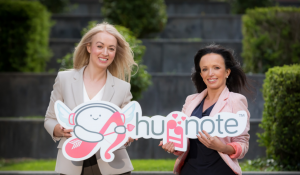 Huggnote founders and sisters holding an image of the Huggnote App logo - which depicts two music notes facing each other as if hugging and character wearing 2022 New Year hat