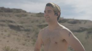 A young shirtless blond man looks out over the Nevada desert
