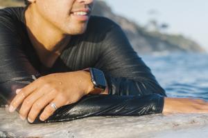 Iš arti vyro paplūdimyje su bangomis už jo, rodančio laikrodį ant riešo
